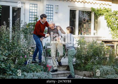 Homme souriant avec son fils aidant le père senior à descendre sur les marches à l'arrière-cour Banque D'Images