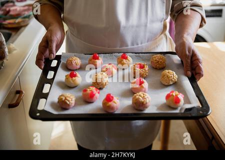 Femme avec tablier tenant des panellets dans la plaque de cuisson à la cuisine Banque D'Images