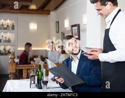 Serveur accueillant qui aide les jeunes hommes avec un menu Banque D'Images