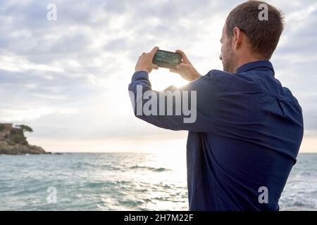 Homme photographiant la mer à la plage avec un smartphone Banque D'Images