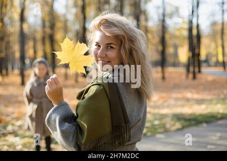 Femme souriante tenant une feuille d'automne dans un parc public Banque D'Images