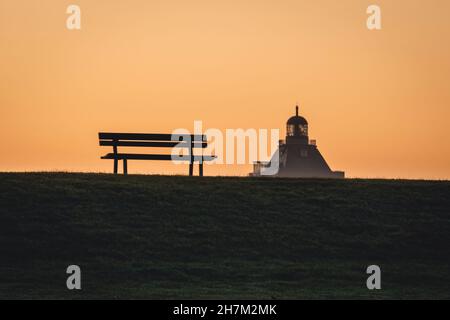 Allemagne, Hambourg, Silhouette du banc de parc vide à moody crépuscule avec le phare de la Grande Tour Neuwerk en arrière-plan Banque D'Images