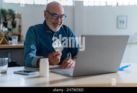 Homme à la retraite souriant avec des médicaments prenant des conseils de médecin sur appel vidéo par ordinateur portable Banque D'Images