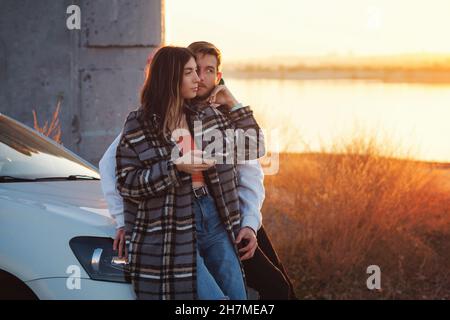 Le voyageur de couple se tient en voiture au coucher du soleil dans la campagne.Elle utilise la carte des applications mobiles dans son smartphone pour trouver le chemin.Les touristes qui vérifient la position dans la carte du smartphone.Mise au point douce Banque D'Images