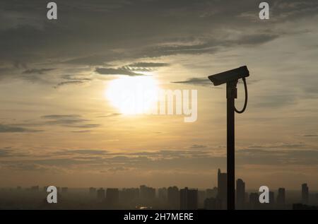 Ombre d'une caméra de surveillance moderne sur fond urbain et gratte-ciel avec soleil criant vif avant le coucher du soleil.Le concept de surveillance Banque D'Images