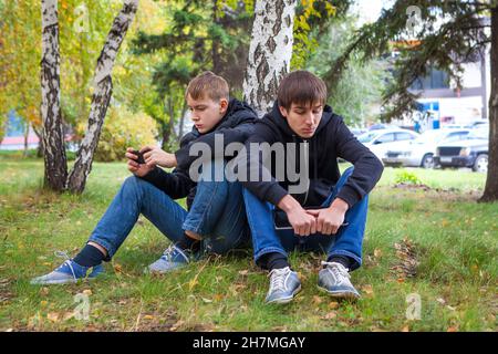 Sad Boys s'assoient sous un arbre dans le parc d'automne Banque D'Images