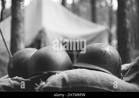 Casques métalliques du soldat d'infanterie de l'armée des États-Unis à la Seconde Guerre mondiale Casques près de la tente de camping dans Forest Camp. Photographie en noir et blanc. Banque D'Images