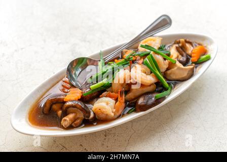 Crevettes sautées, champignons shiitake ou champignons chinois avec sauce aux huîtres dans une belle assiette ovale sur la table en pierre blanche, image rapprochée Banque D'Images