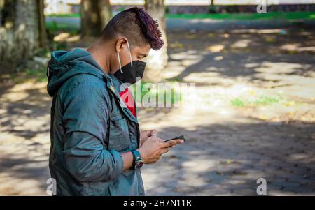 Homme avec un masque texting avec son téléphone, jeune homme avec un masque texting avec son téléphone cellulaire, gros plan d'un jeune homme avec un masque texting Banque D'Images