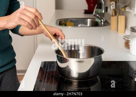 Les mains des jeunes hommes remuent la sauce pour spaghetti sur la table de cuisson en céramique Banque D'Images