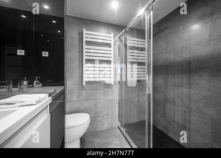 Enceinte de douche avec radiateur sur le mur d'une salle de bains avec carreaux gris brillant et noirs Banque D'Images