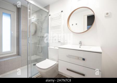 Salle de bains moderne avec mobilier, lavabo blanc et miroir rond Banque D'Images