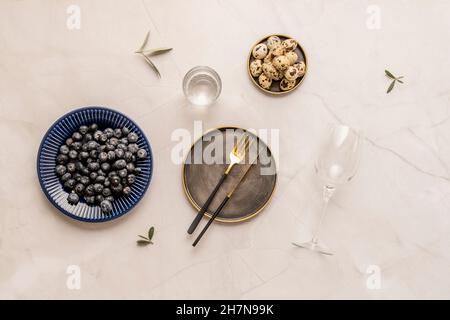 Ensemble d'assiettes, de verres avec eau et de verres.Œufs de caille dans une assiette d'époque et feuilles d'olive sur une table en marbre blanc Banque D'Images