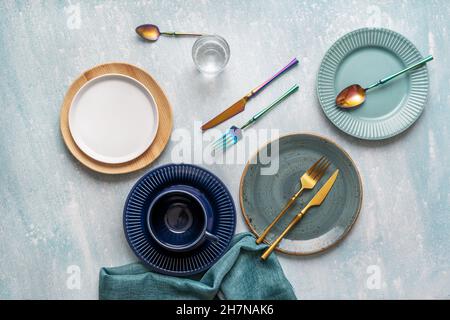 Ensemble de magnifiques assiettes colorées avec tissu bleu et couverts irisés et dorés sur fond bleu ciel Banque D'Images