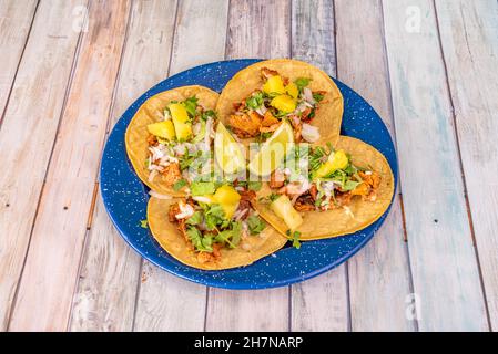 Assiette métallique bleue émaillée de bleu avec un ensemble de tacos al pasteur avec ragoût de viande, oignon, mangue, lime et coriandre Banque D'Images