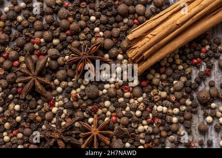 Image en gros plan avec des graines de poivre multicolores, des bâtonnets de cannelle et des graines d'anis étoilé sur une table en bois Banque D'Images