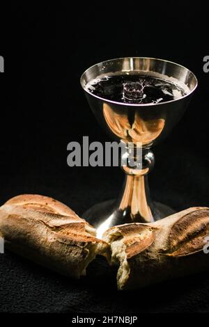 Calice de vin et pain fraîchement cuit sur un fond et une surface sombres - Sainte Communion Banque D'Images