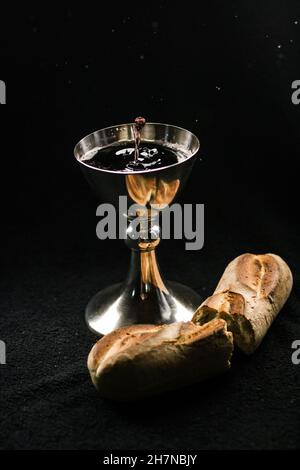 Calice de vin et pain fraîchement cuit sur un fond et une surface sombres - Sainte Communion Banque D'Images