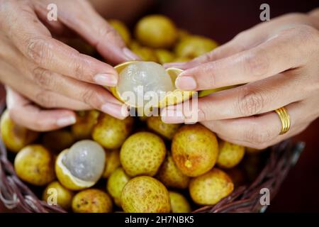 fruits de longan à éplucher à la main humaine dans un panier en osier Banque D'Images