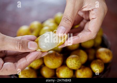 fruits de longan à éplucher à la main humaine dans un panier en osier Banque D'Images