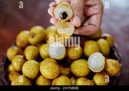 fruits de longan à éplucher à la main humaine dans un panier en osier Banque D'Images