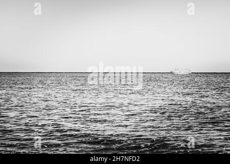 Photographie noir et blanc.Seul bateau blanc ou bateau dans la mer silencieuse ou l'eau de l'océan Banque D'Images