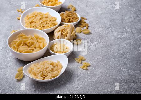 Variété de pâtes italiennes crues dans un bol blanc sur fond de béton gris Banque D'Images