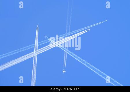 De nombreux avions à réaction de passagers à distance volent en haute altitude sur un ciel bleu clair laissant derrière eux une trace blanche de fumée de contrail.Centre de transport aérien très fréquenté Banque D'Images