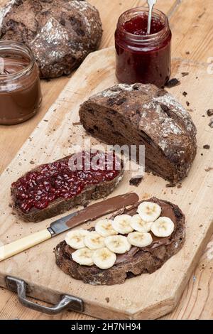 Pain Sourdough au chocolat avec tartinade aux noisettes au chocolat, tranché de banane et de confiture de framboise sur une planche de bois Banque D'Images