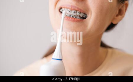 Souriante jeune femme méconnaissable avec des bretelles nettoyant ses dents à l'aide d'un irrigateur oral. Banque D'Images