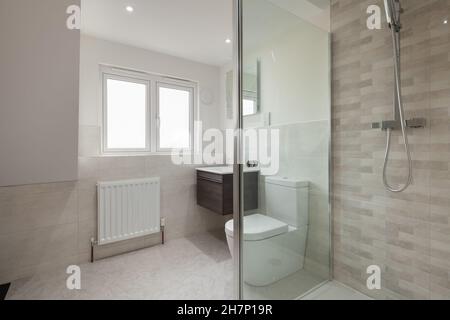 Salle de bains attenante moderne dans la nouvelle maison mise en vente avec cabine de douche, toilettes et lavabo mural Banque D'Images