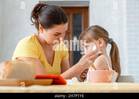 Mère nourrit sa fille avec de la nourriture de la cuillère et essuie son visage avec serviette.Soins maternels de l'enfant fille de style de vie réel déjeuner de mécontent Banque D'Images