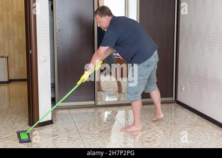 grand homme avec un sourire moche les sols dans son appartement en aidant sa femme à nettoyer. Banque D'Images