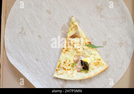 Une tranche de pizza dans une grande boîte en carton.La dernière tranche de pizza aux herbes et au bacon. Banque D'Images