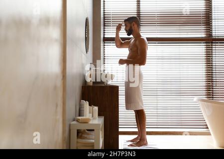 Vue latérale d'un jeune homme regardant dans le miroir se brossant les cheveux Banque D'Images
