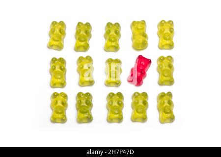 Des rangées d'ours verts délicieux dans lesquels un gars rouge se comporte différemment du concept de l'individualité et étant différent isolé sur un fond blanc Banque D'Images