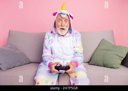 Photo de l'homme funky impressionné pensionné unicorn dors-bien canapé tenant un arrière-plan de couleur rose isolé de la PlayStation Banque D'Images