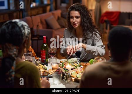 Jeune femme assise à la table en train de manger de la salade et de parler à ses amis Banque D'Images