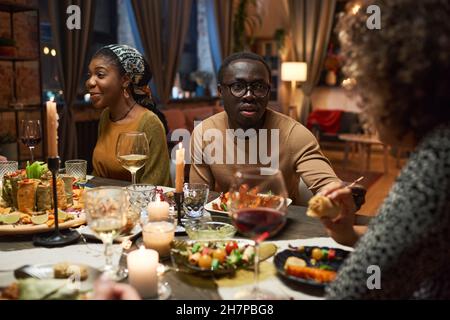 Un jeune homme africain en lunettes parlant à ses amis pendant le dîner à la table Banque D'Images