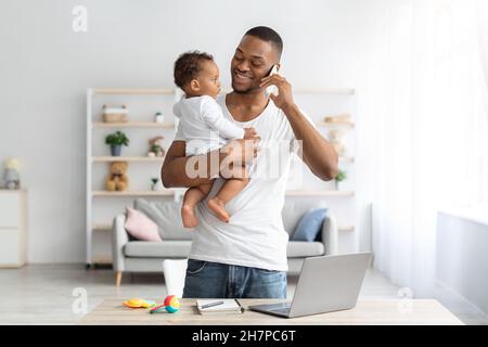 Concept multitâche.Jeune Noir tenant bébé et parlant sur téléphone portable Banque D'Images