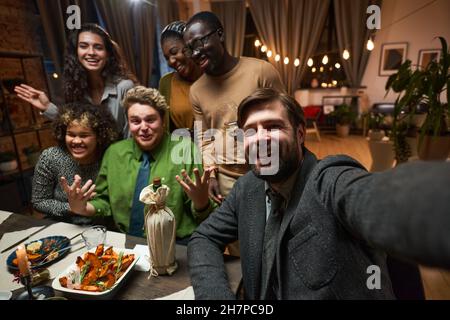 Portrait d'un groupe d'amis heureux souriant à l'appareil photo tout en étant assis à la table dans le salon Banque D'Images