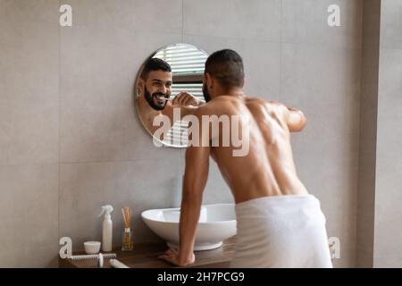 Joyeux jeune homme arabe utilisant la brosse à dents dans la salle de bains Banque D'Images