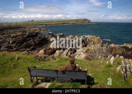 Femme assise sur le banc et vue sur l'île de Whithorn Bay & St Ninois, Dumfries & Galloway, Écosse Banque D'Images