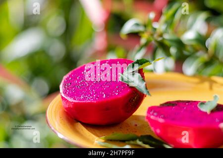 Des couleurs vives de fruits Dragon coupés en deux sur une assiette jaune avec des fleurs et des feuilles pour le décor. Banque D'Images