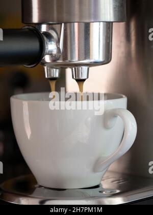 Dose verticale d'un café versé dans une tasse en céramique blanche à partir d'une machine à café Banque D'Images