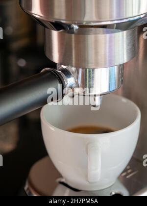 Gros plan d'un café versé dans une tasse en céramique blanche à partir d'une machine à café Banque D'Images