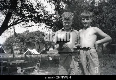 1938, historique, camp de scouts, debout ensemble à l'extérieur, deux jeunes cub souts ou hiboux, avec un pudding de riz - trop cuit!- fabriqué dans la cuisine du camp, Angleterre, Royaume-Uni. Banque D'Images