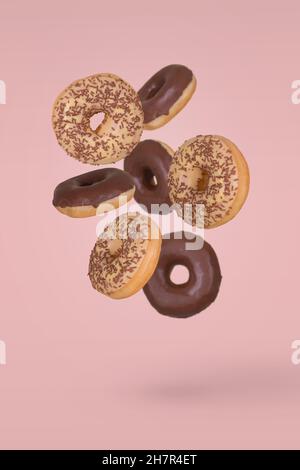 Beignets recouverts de chocolat noir et blanc et parsemés de chapelure de chocolat volant sur fond rose vif.Dessert créatif et doux conceps Banque D'Images