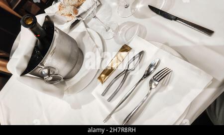 Table de restaurant avec vaisselle argentée et une bouteille de vin dans un seau rempli de glace Banque D'Images