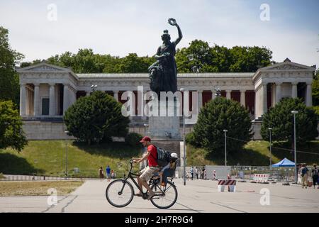 Homme avec enfant dans le siège de sécurité à vélo après la statue de Bavière et Ruhmeshalle (Hall of Fame) onTheresienwiese à Munich, Bavière, Allemagne. Banque D'Images